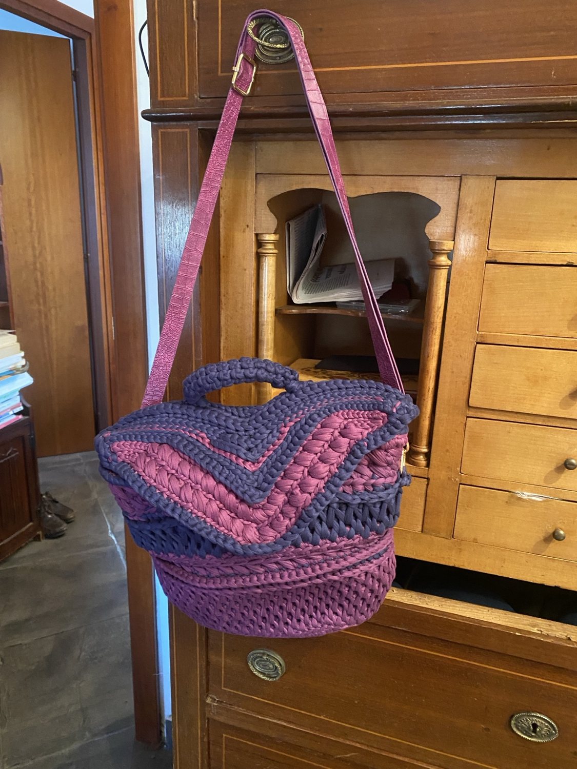 Borsa rosa e viola con tracolla, appesa davanti a un mobile